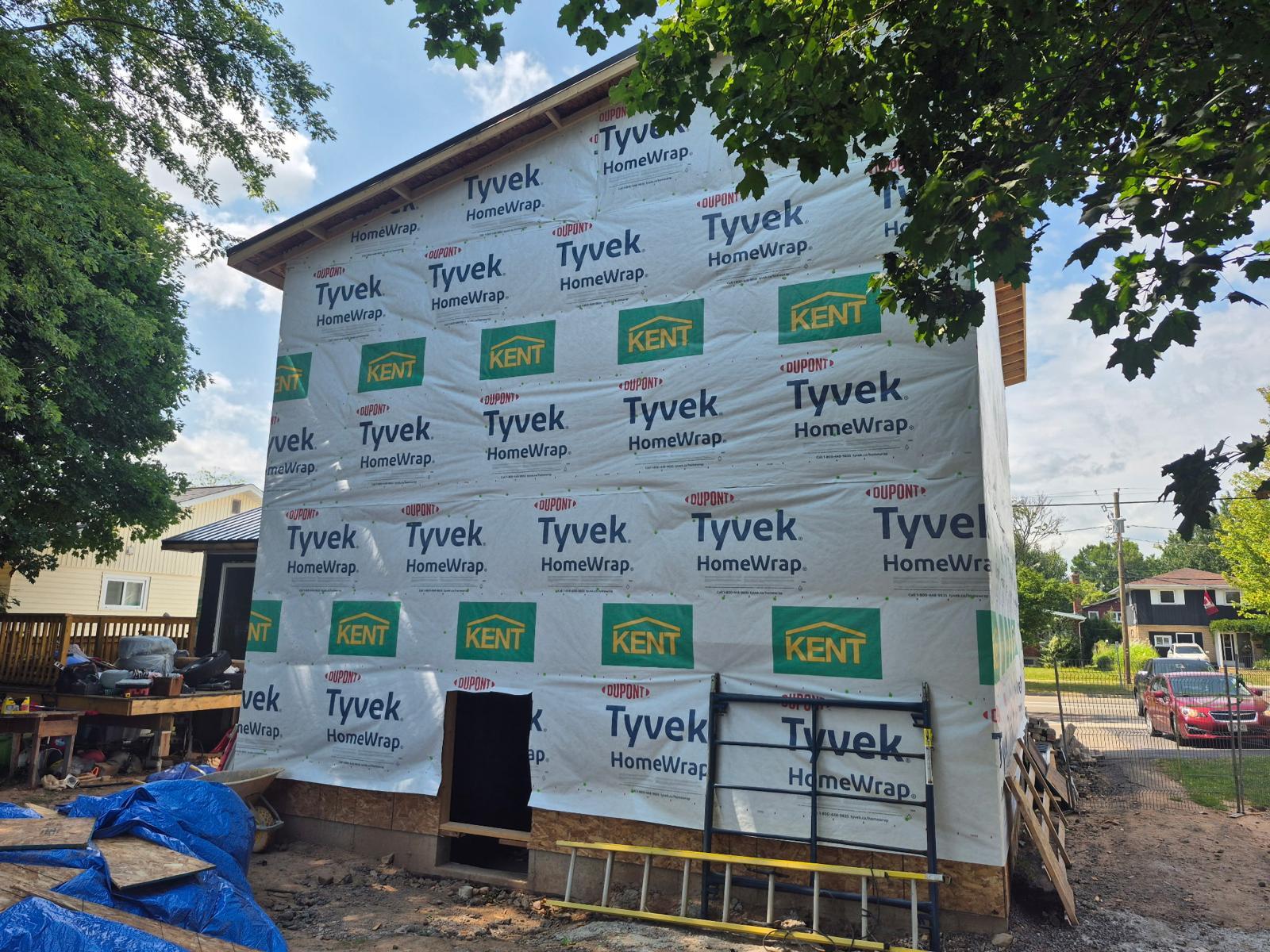 A second-storey addition wrapped in housewrap, with the original brick being removed from the main floor below