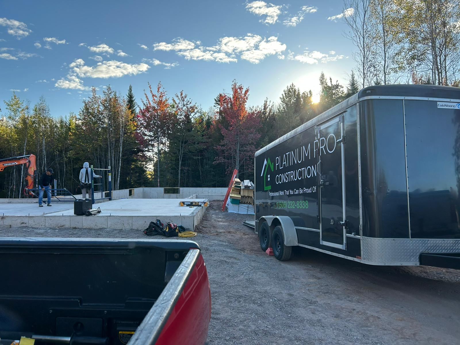 The Platinum Pro Construction trailer parked beside a poured foundation while two crew members work on the slab