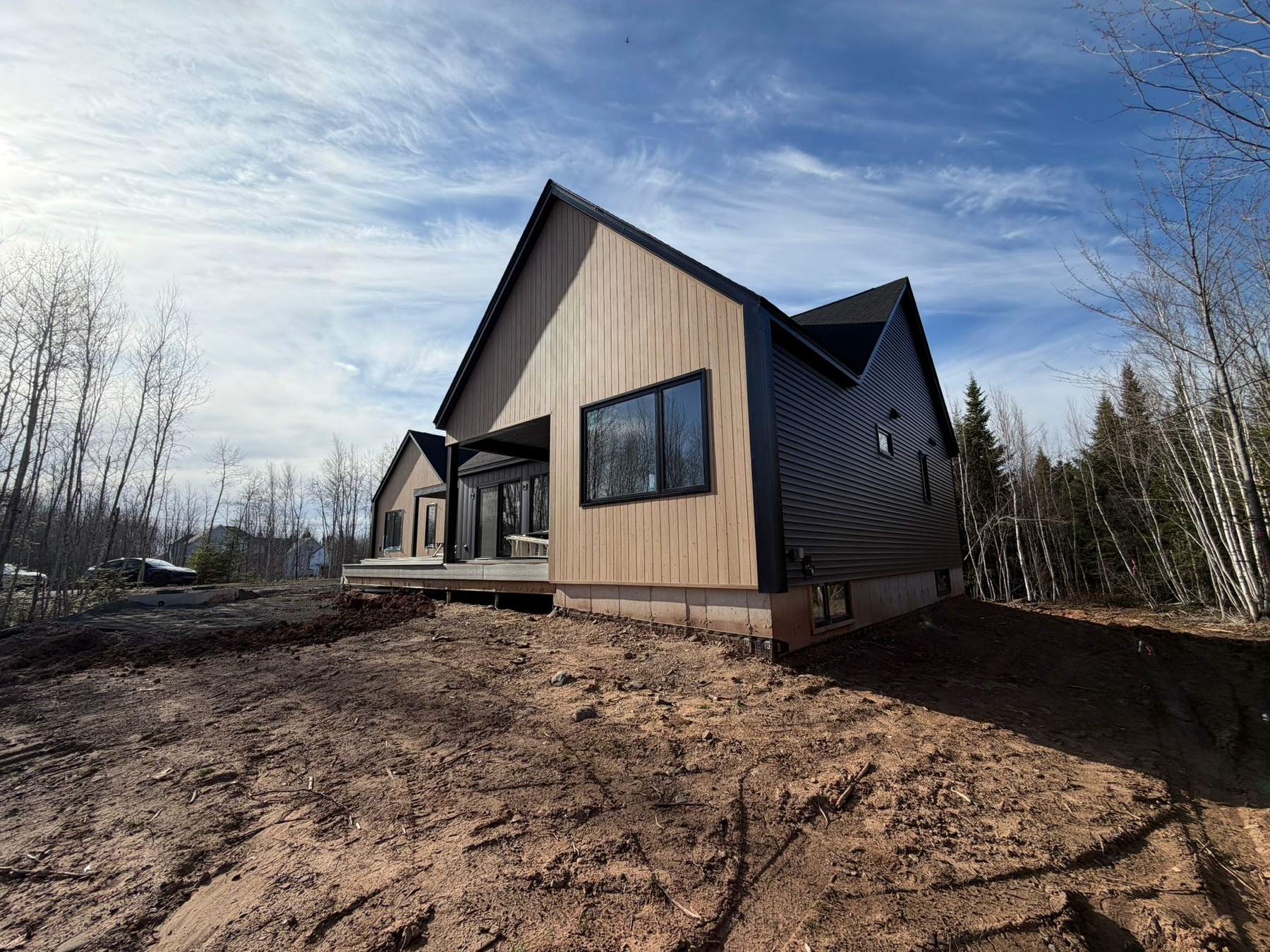 A newly built custom home with cedar-toned board-and-batten and dark horizontal siding, on a lot still being graded