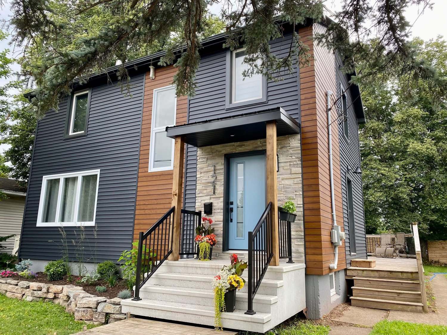 A renovated two-storey home with charcoal siding, cedar accent panels, a stone entry surround and a new covered porch