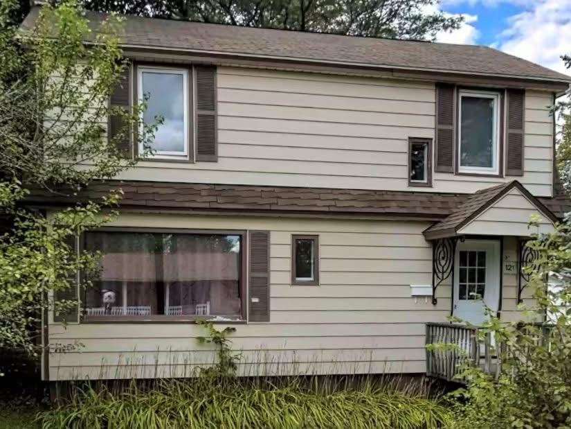 Front of a house before renovation, with dated cream siding and brown shutters