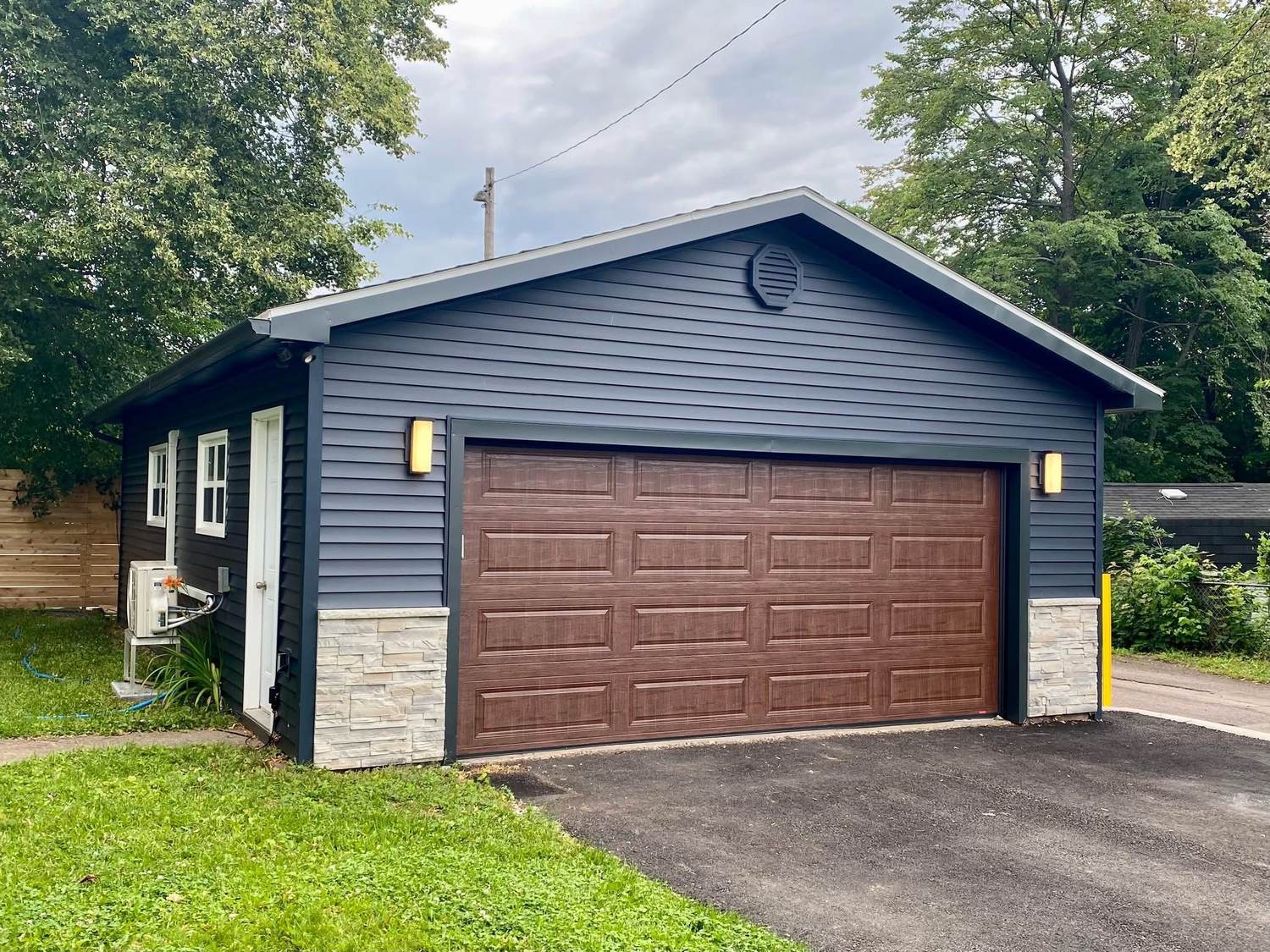 A detached garage after renovation, resided to match the house with a stone skirt and new overhead door